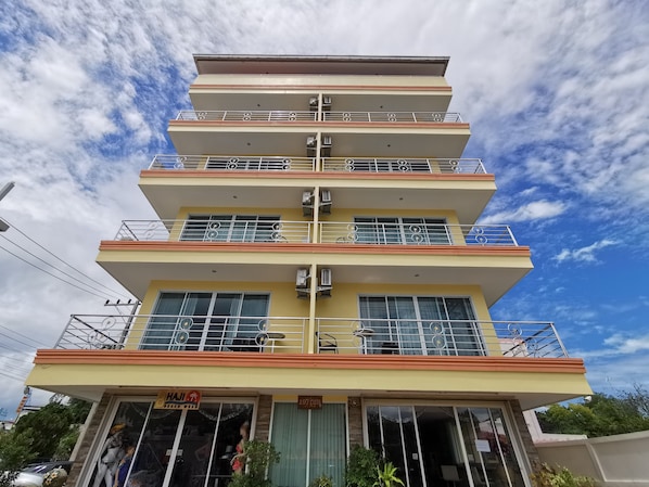 A multi-story hotel with balconies, air conditioning units, and a beachwear sign.