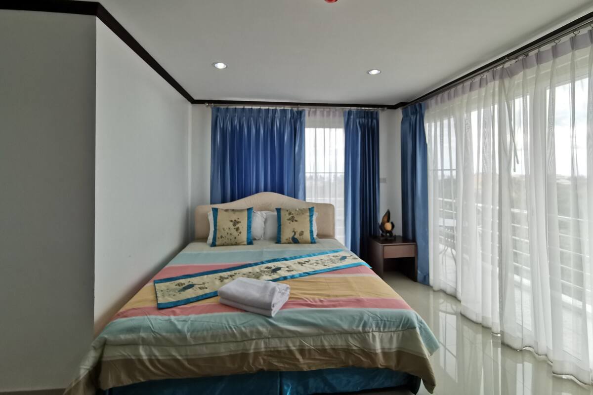 Un dormitorio con cama, cortinas, mesita de noche y una lámpara en el techo.