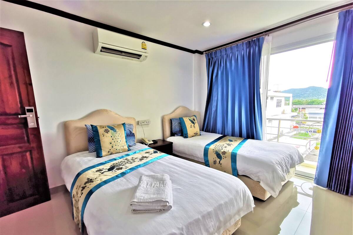 Habitación de hotel con dos camas, una ventana con cortinas azules, un equipo de aire acondicionado y vistas al exterior.