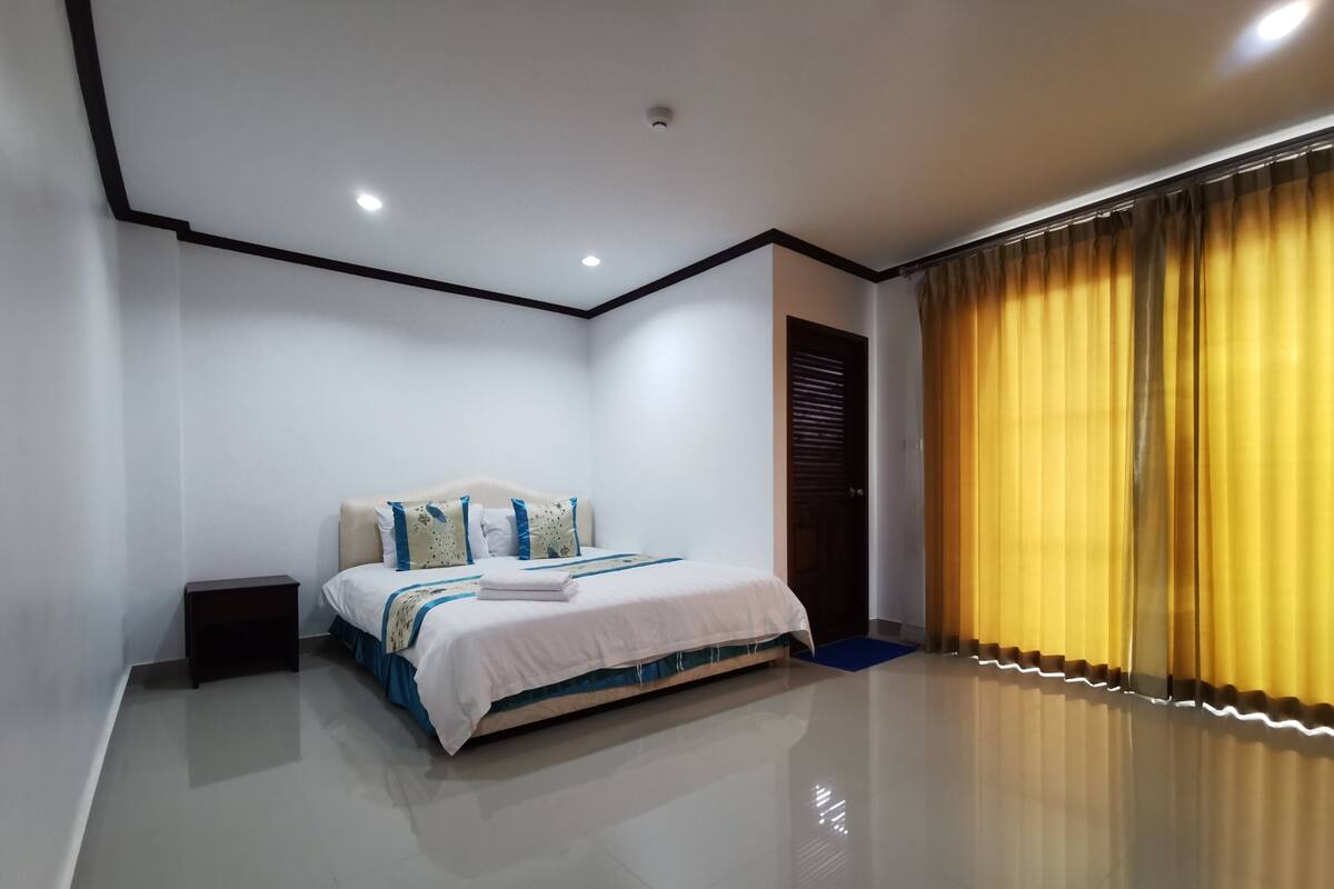 Un dormitorio moderno con cama, mesita de noche y un amplio ventanal con cortinas.