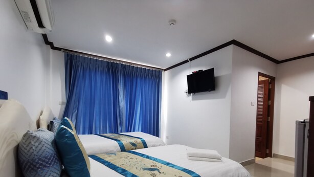 A hotel room with two beds, a flat-screen TV mounted on the wall, a ceiling-mounted air conditioner, and a wooden door. - Baan Pattamaporn Hotel (Hua Hin)