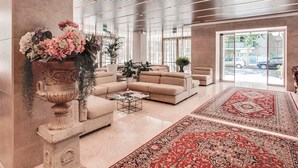 A spacious lobby with a large red patterned rug, beige sofas, and a decorative urn with flowers. - Hotel Ambasciatori (Cesenatico)