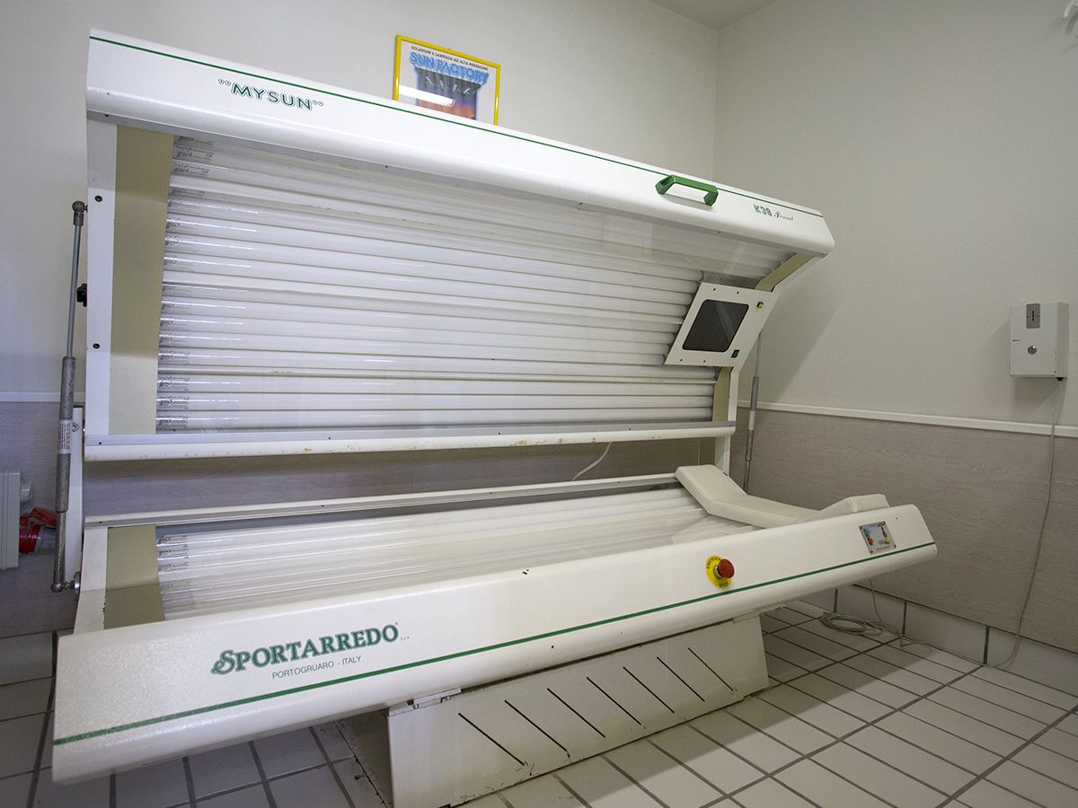 Une salle contenant du matériel médical, où se trouve un grand appareil de bronzage blanc et fixe, portant les inscriptions « SPORTARREDO » et « MYSUN ».