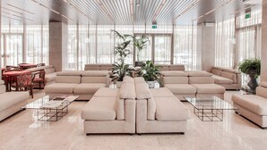 A spacious, modern lounge area with a large sectional sofa, a glass coffee table, and several potted plants. - Hotel Ambasciatori (Cesenatico)