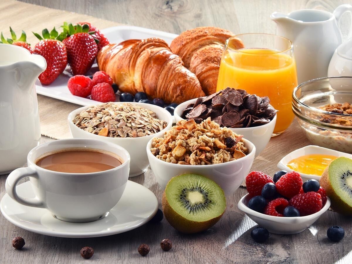 A breakfast setting with croissants, strawberries, blueberries, kiwi, and various cereals.