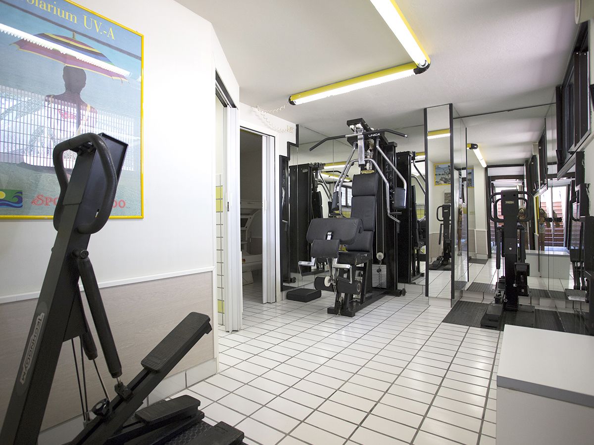 Ein Fitnessraum mit Trainingsgeräten, einem Spiegel und einem Wandplakat.