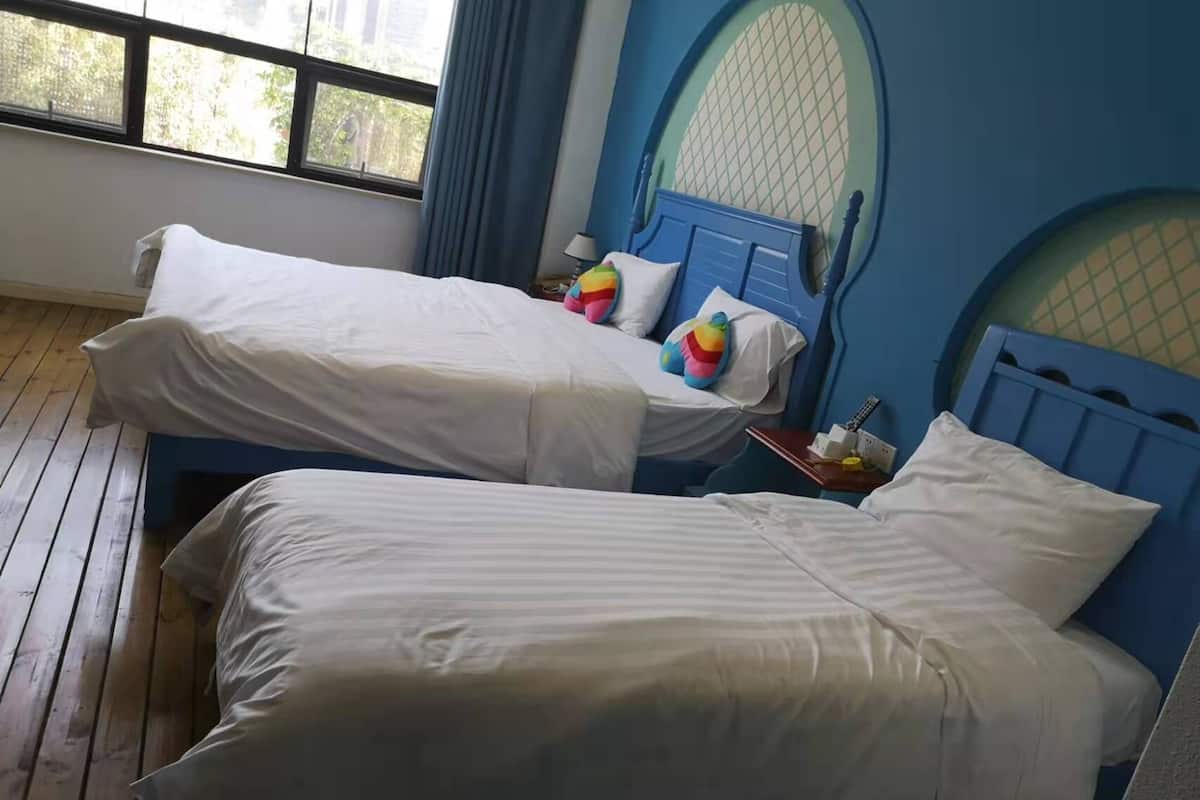A room with two beds, each with white bedding and colorful pillows. There is a window with a view of trees outside.