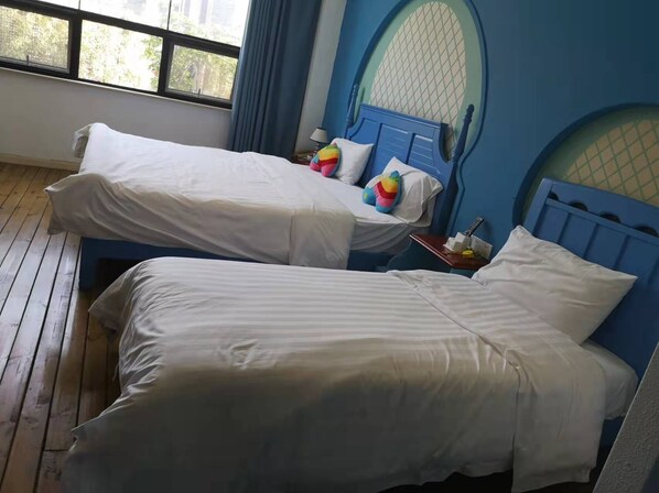 Una habitación con dos camas, cada una con ropa blanca y almohadas de colores. Se ve una ventana con vista a árboles.