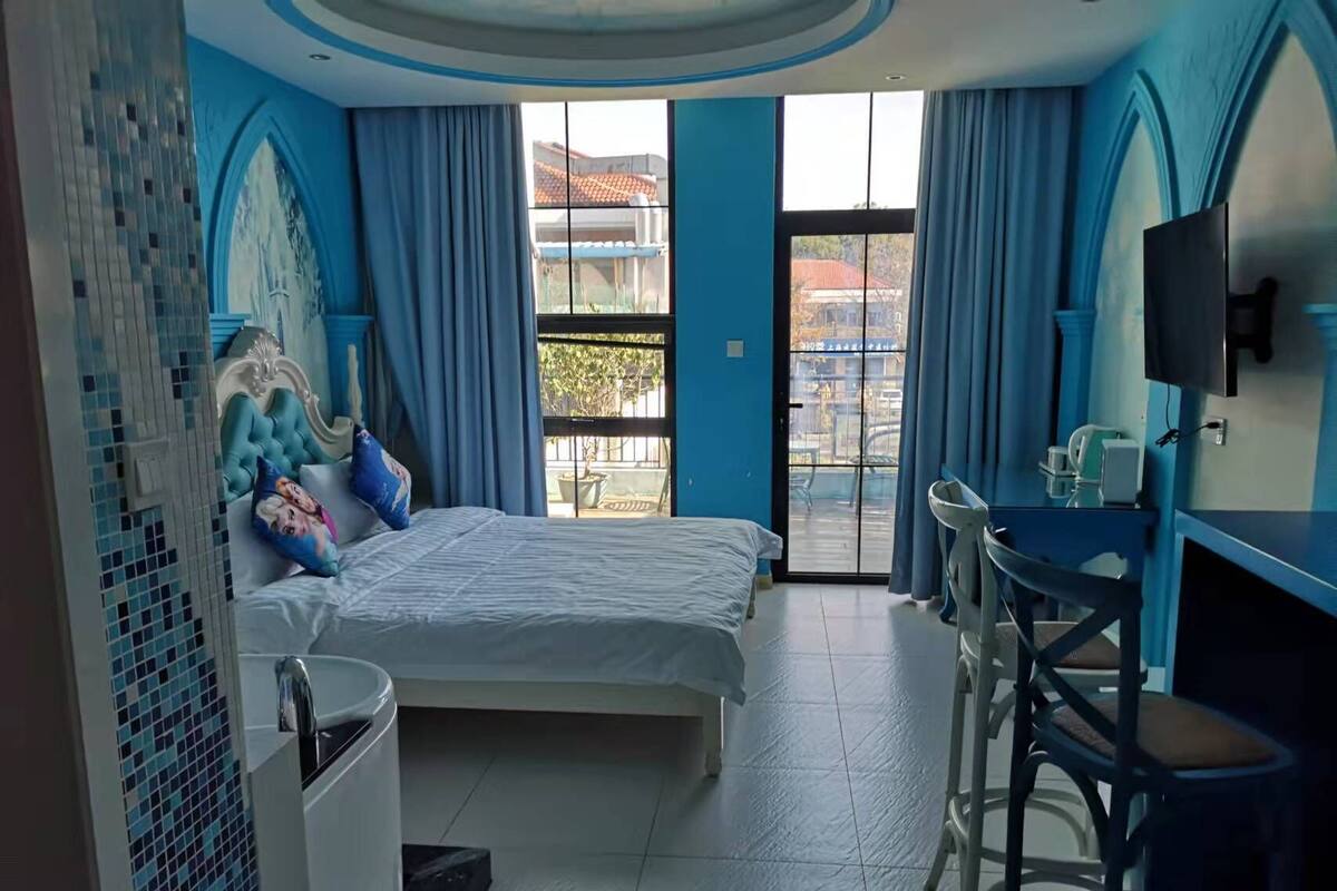 A hotel room with a bed, a desk, a chair, a TV, and a balcony with a view.