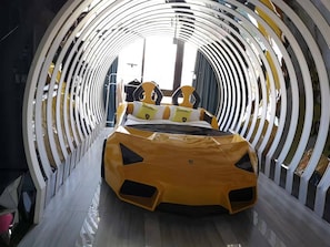 Un coche deportivo amarillo en un espacio tipo túnel con una cama y una silla.