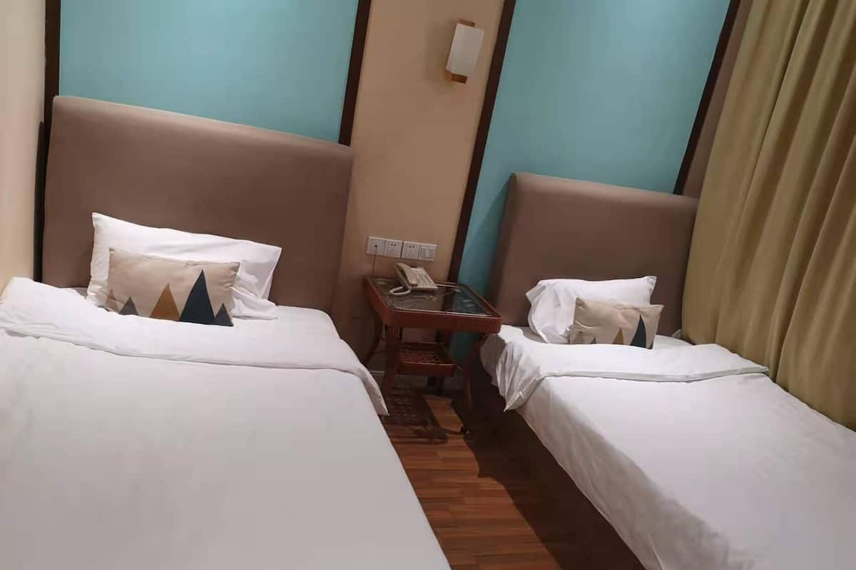 A hotel room with two single beds, a small table with a phone, and a wall-mounted light.