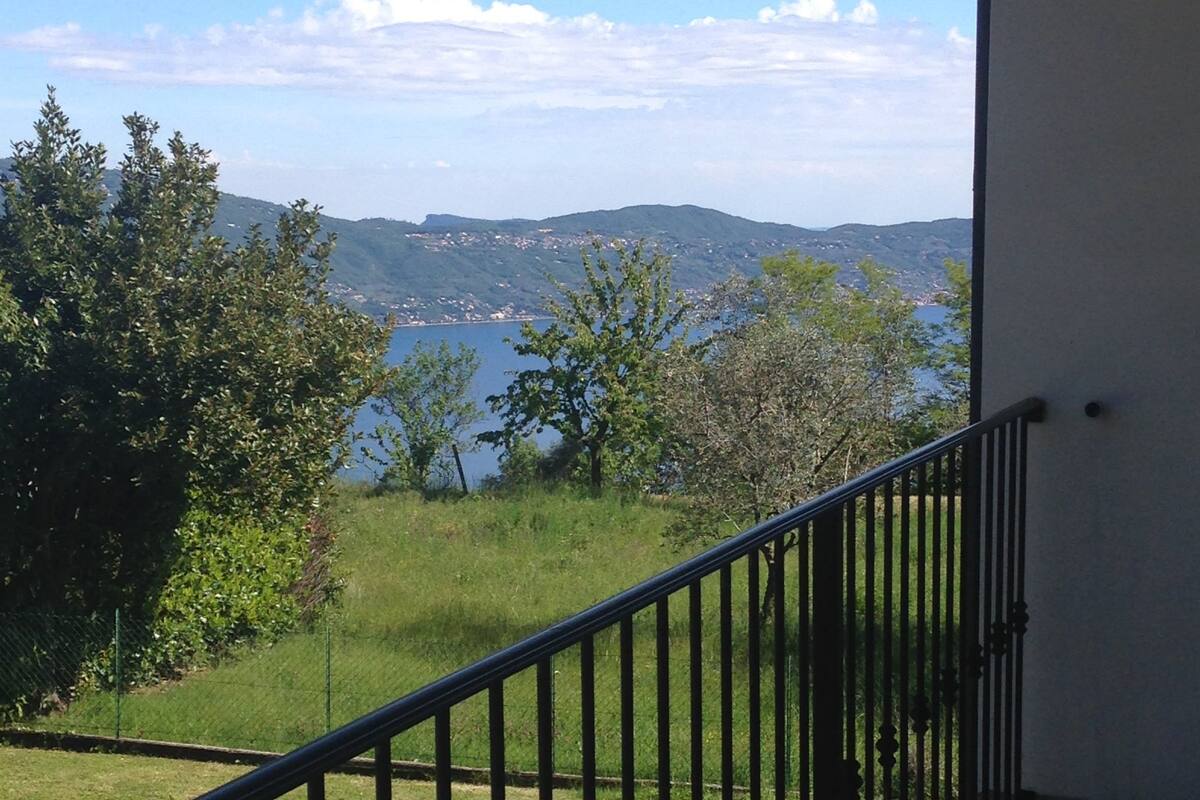 A balcony with a metal railing overlooking a grassy area and a body of water.