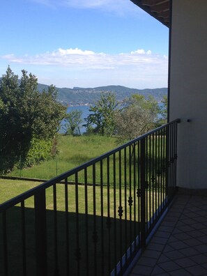 A balcony with a metal railing overlooking a grassy area and a body of water. - Garni Marika (Gargnano)
