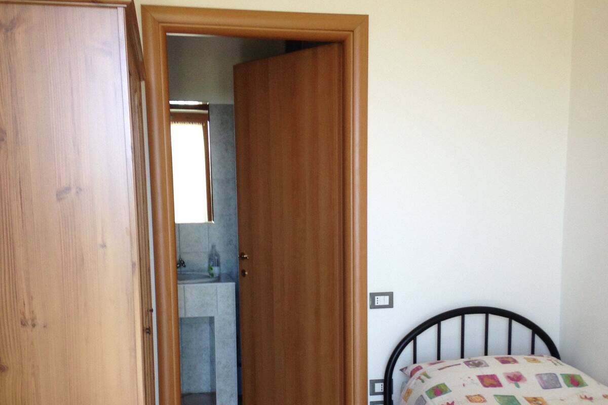 A bedroom with a bed, a wooden door, and a bathroom visible through an open door.