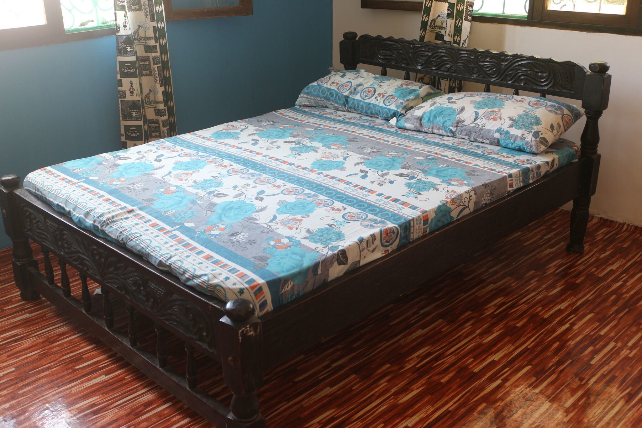 Un lit avec une couvre-lit à motifs et des oreillers, une tête de lit en bois foncé et un plancher en bois.