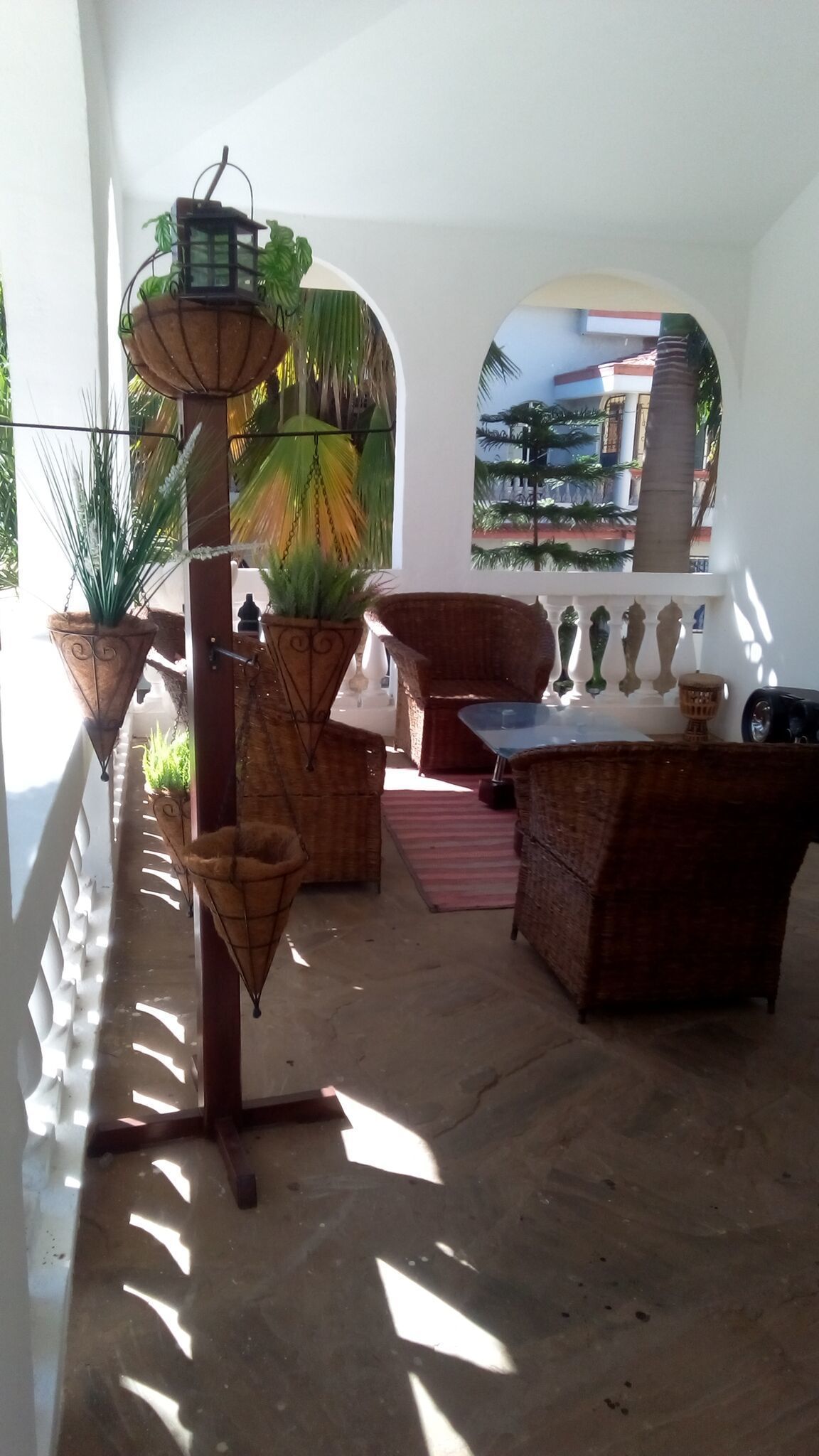 A covered outdoor seating area with wicker furniture, potted plants, and a view of a building through an archway.