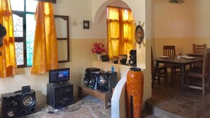 A living room with a TV, speakers, and a dining area with a table and chairs. - Akogo House (Mombasa)