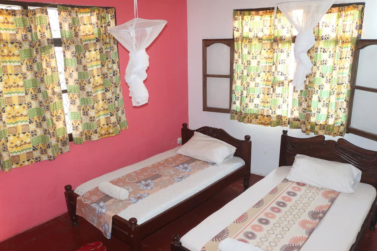 Una habitación con dos camas individuales, una mosquitera y cortinas estampadas.
