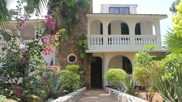 A two-story building with a balcony, surrounded by lush greenery and flowering plants. - Akogo House (Mombasa)