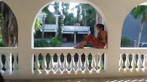 A person sitting on a balcony with a white balustrade, overlooking a building and greenery. - Akogo House (Mombasa)