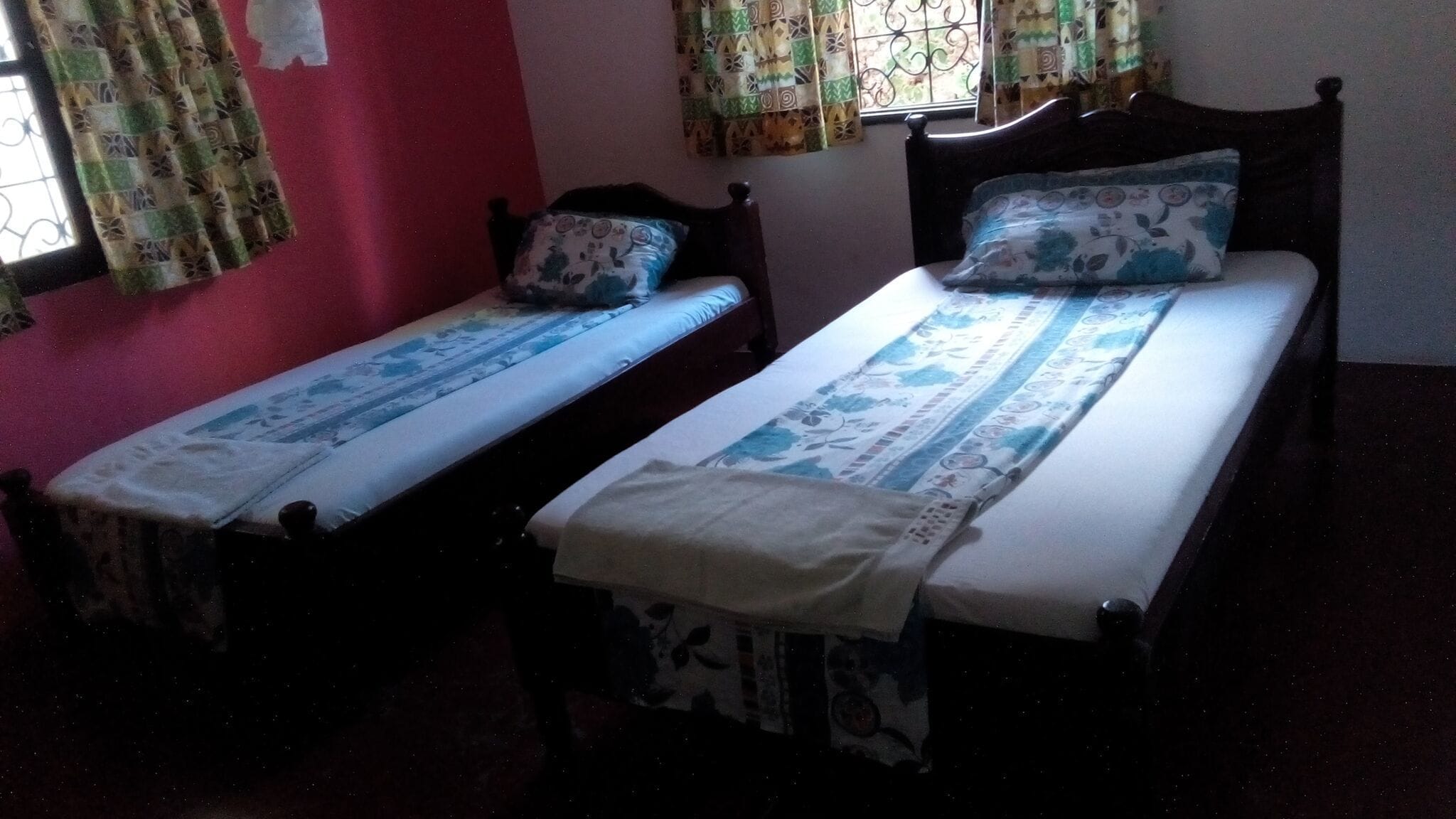 Dos camas individuales con cubrecamas estampadas en una habitación con pared roja y cortinas con diseño.