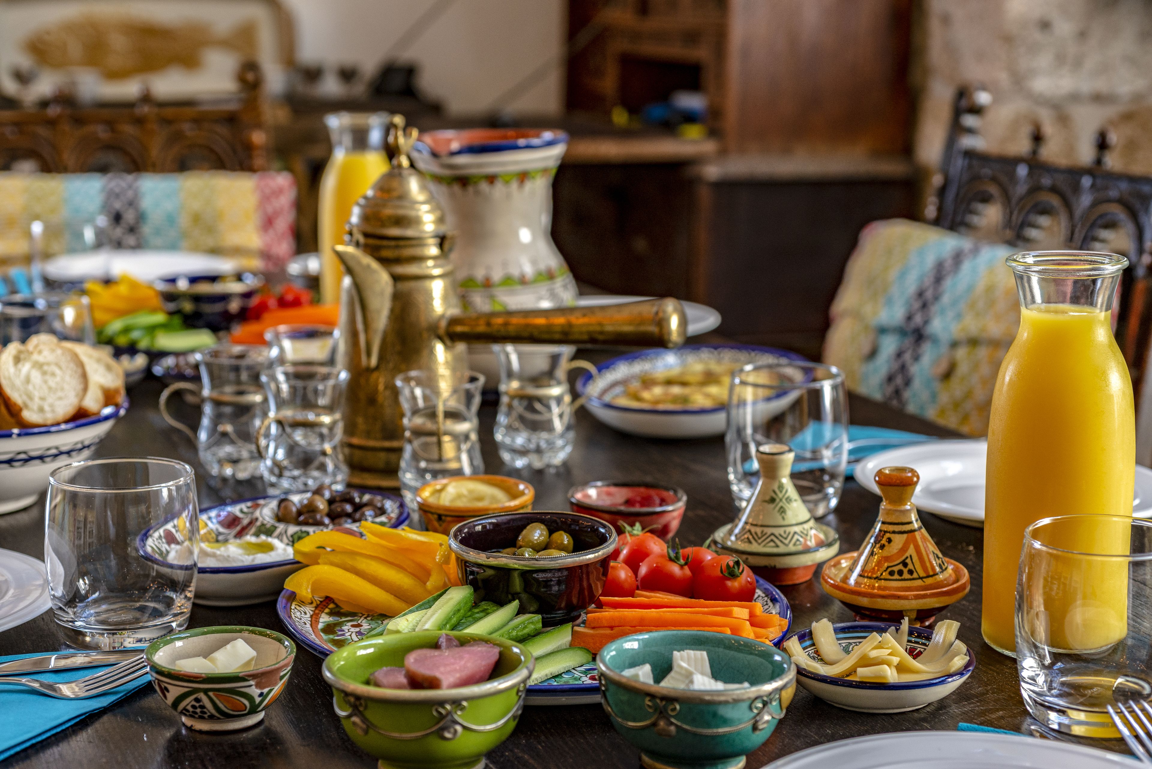 Een gedekte tafel met diverse gerechten, waaronder brood, groenten en een karaf sinaasappelsap.