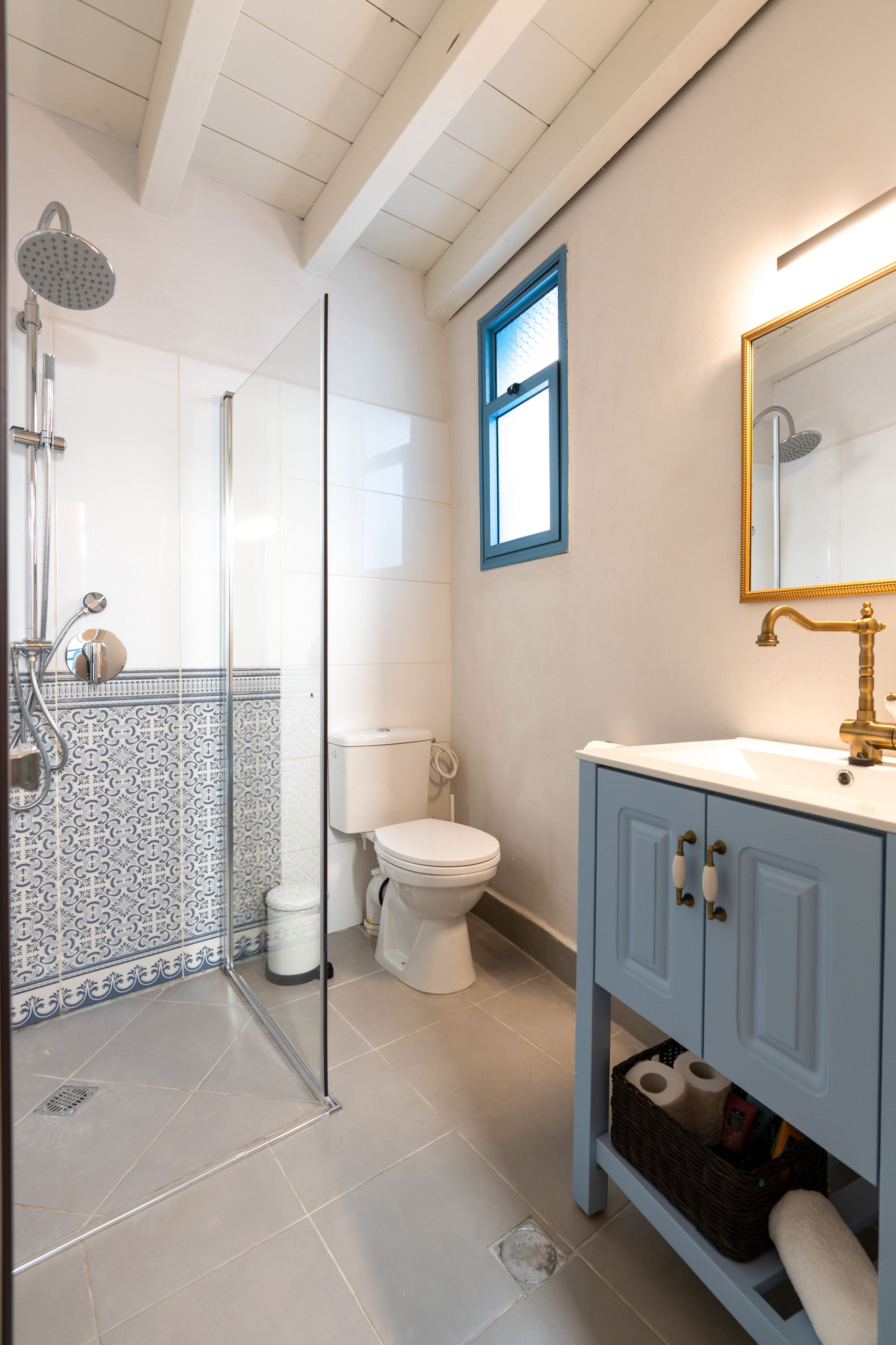 Baño con ducha de vidrio, inodoro, lavamanos con grifo dorado y espejo con marco dorado.
