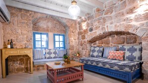 Una habitación acogedora con paredes de piedra, un sofá azul con cojines estampados, una mesa de centro de madera y una mesita auxiliar con una lámpara.