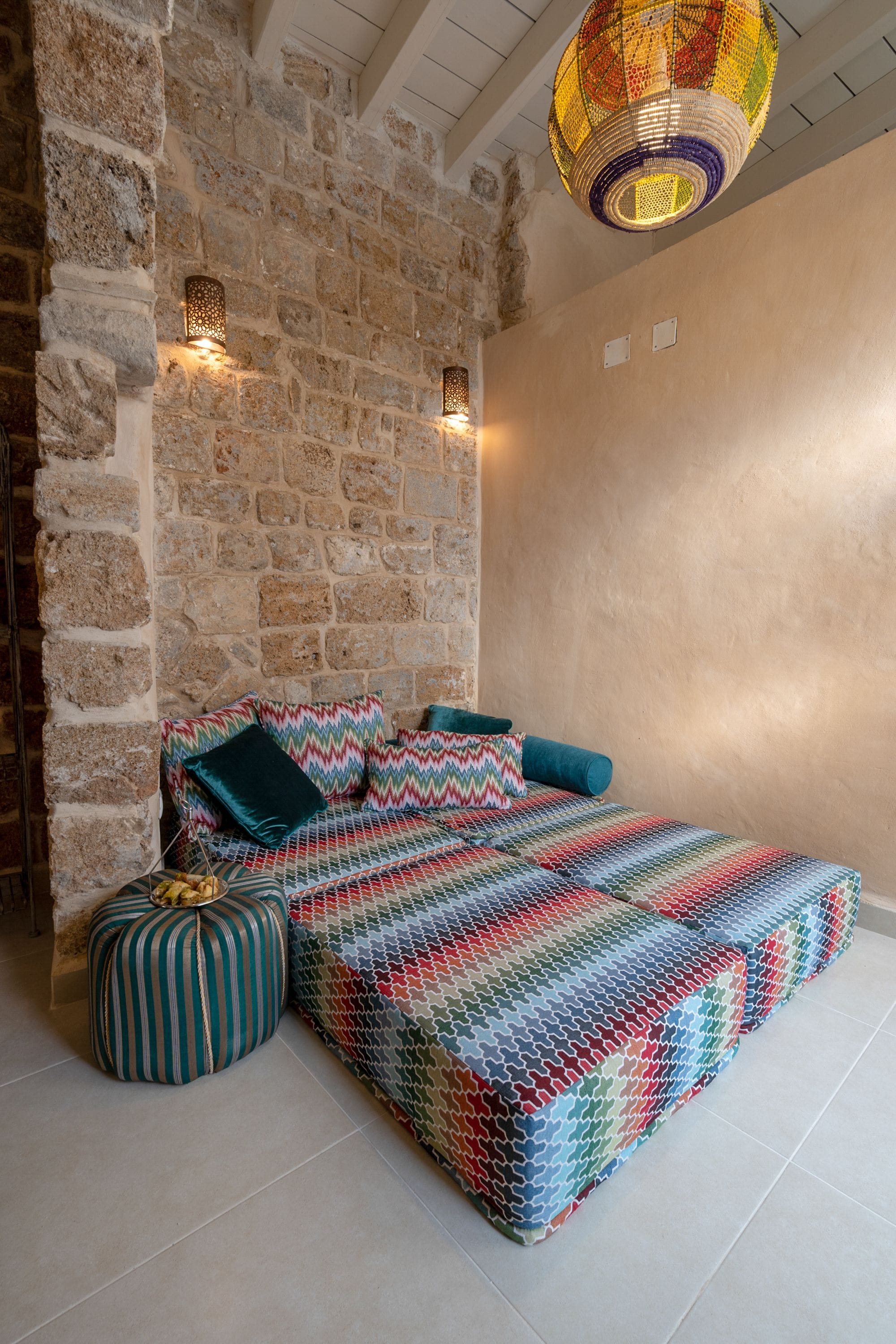 A room with a stone wall, a bed with colorful bedding, and a hanging light fixture.