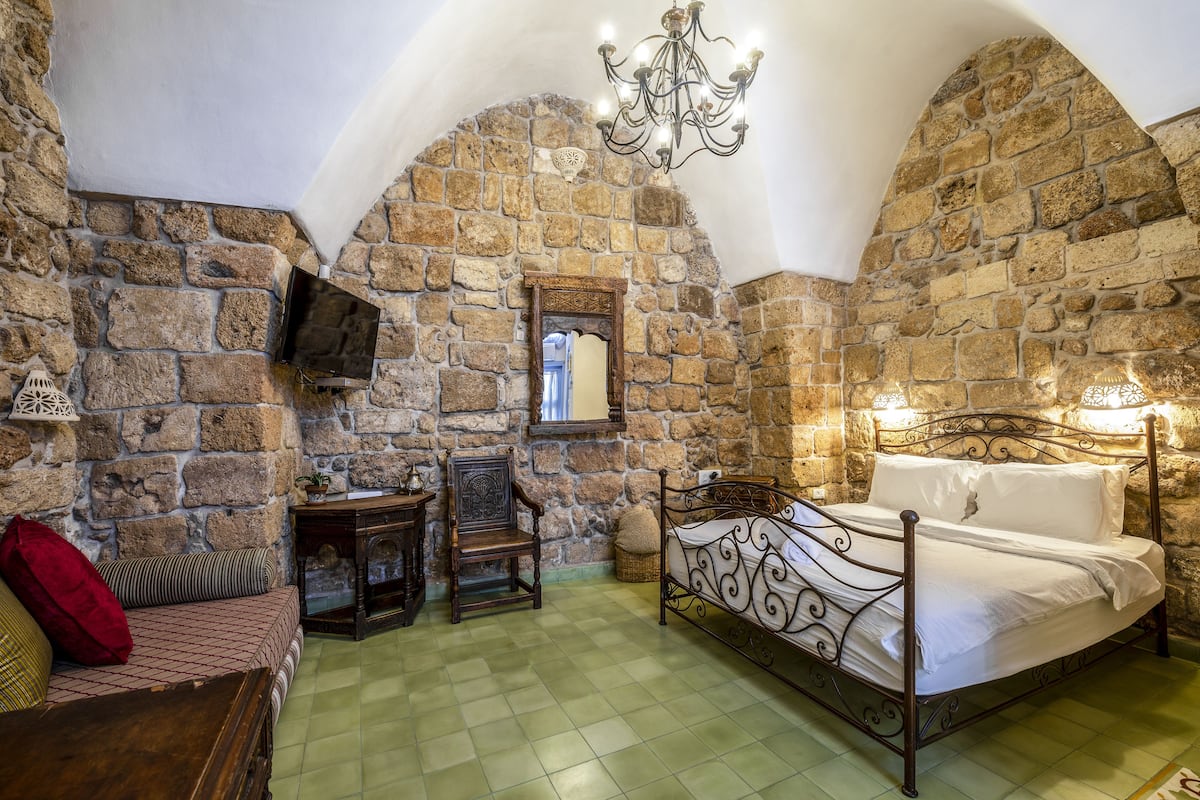 A stone-walled bedroom with a bed, a chair, a small table, and a television.