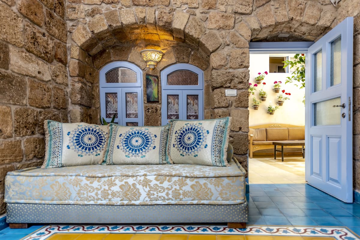 A stone-walled room with a cushioned bench, a door, and a wall-mounted light fixture.