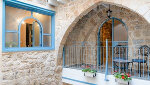 Un edificio de piedra con un balcón, una ventana con detalles azules y una barandilla de metal.