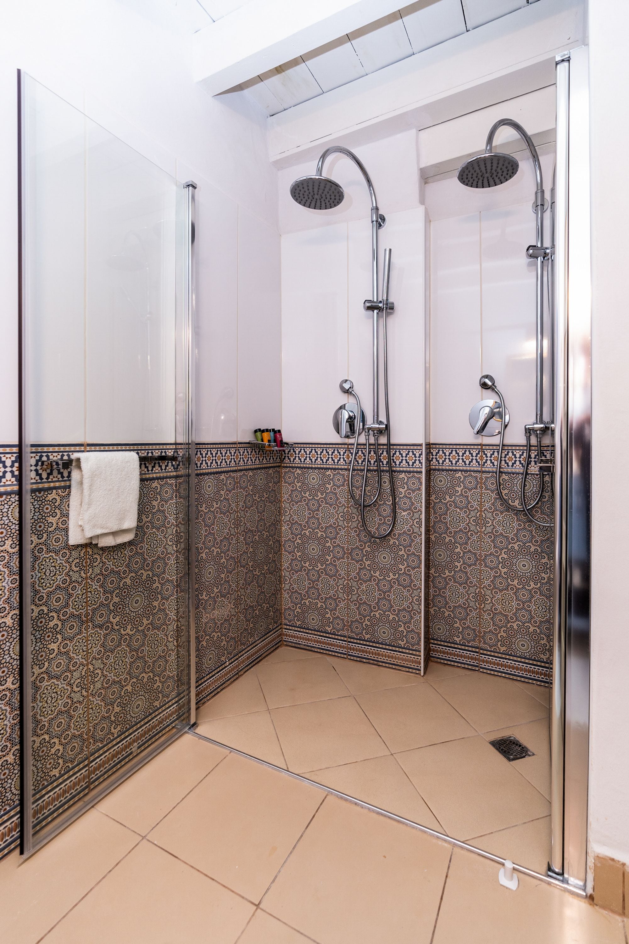 Un bagno moderno con cabina doccia in vetro, piastrelle decorate e un asciugamano bianco appeso al muro.