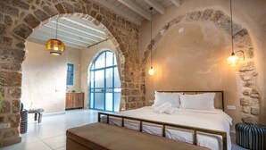 Un dormitorio con pared de piedra, una cama con ropa blanca, un banco y una lámpara colgante.