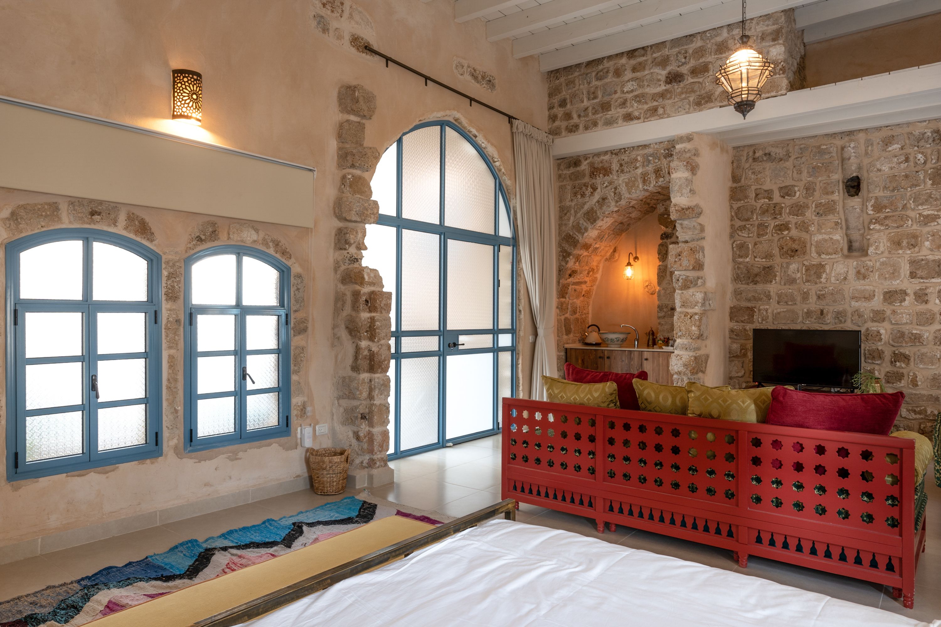 Una habitación con paredes de piedra, una cama, un banco rojo y un televisor.