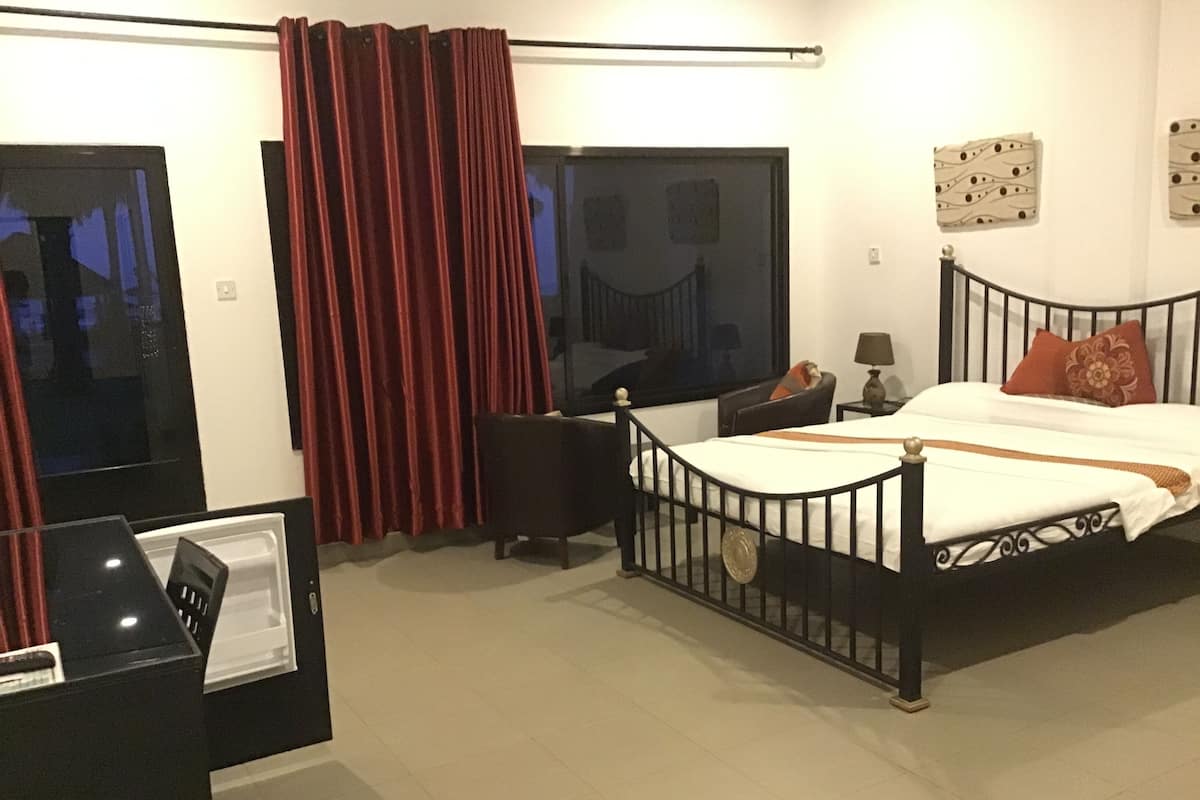 A hotel room with a bed, a desk, a chair, a window with curtains, and a wall with artwork.