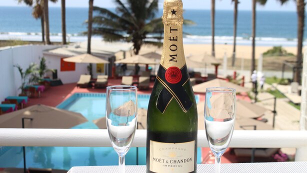 A bottle of Moët & Chandon champagne and two glasses on a table with a pool and beach view.