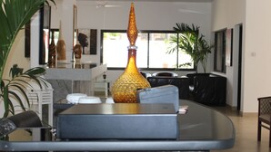 A modern interior with a glass table, a decorative golden vase, and a view of the outdoors through large windows.