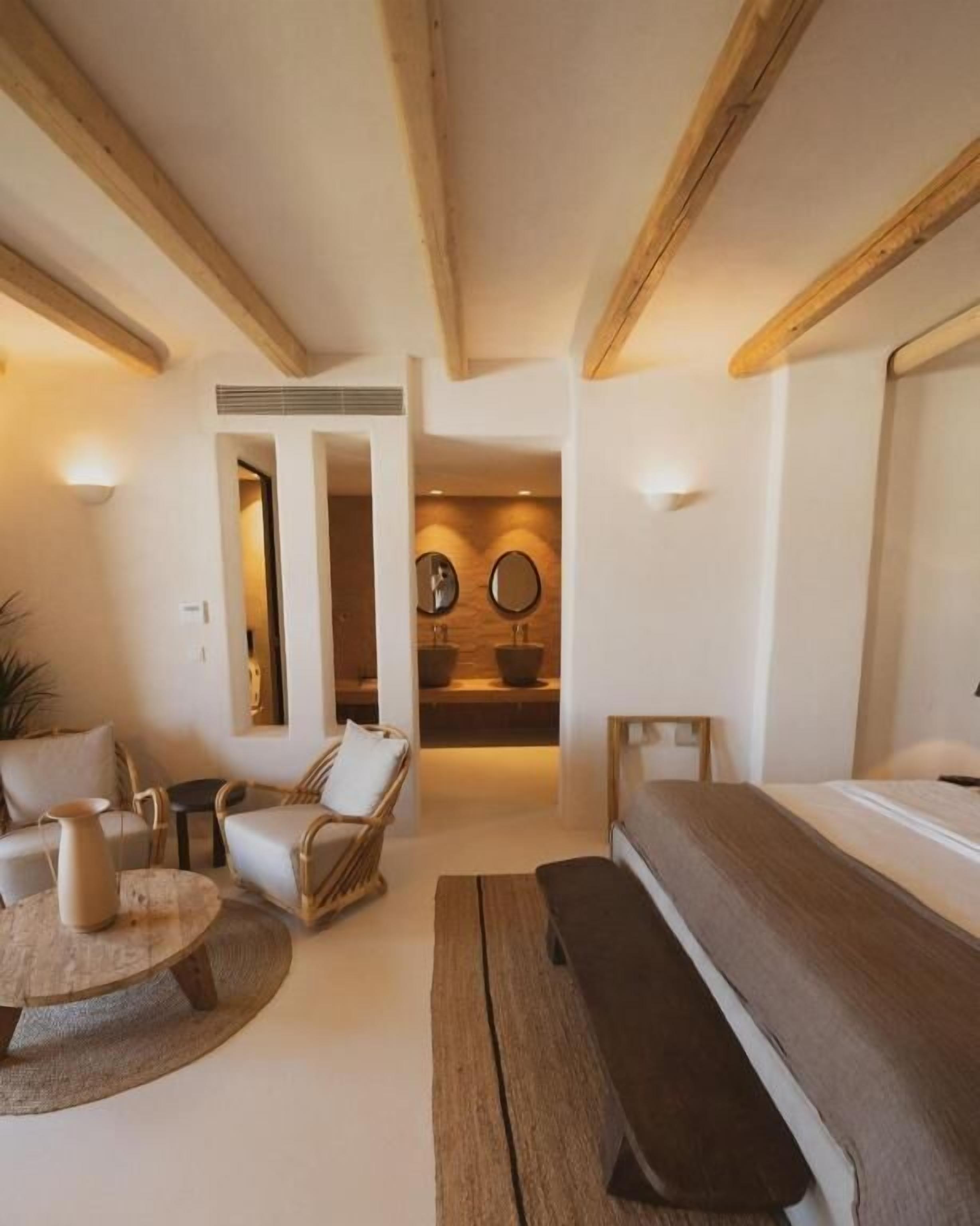 A modern, well-lit room with a wooden ceiling, a bed, a bench, a round table, and two chairs.