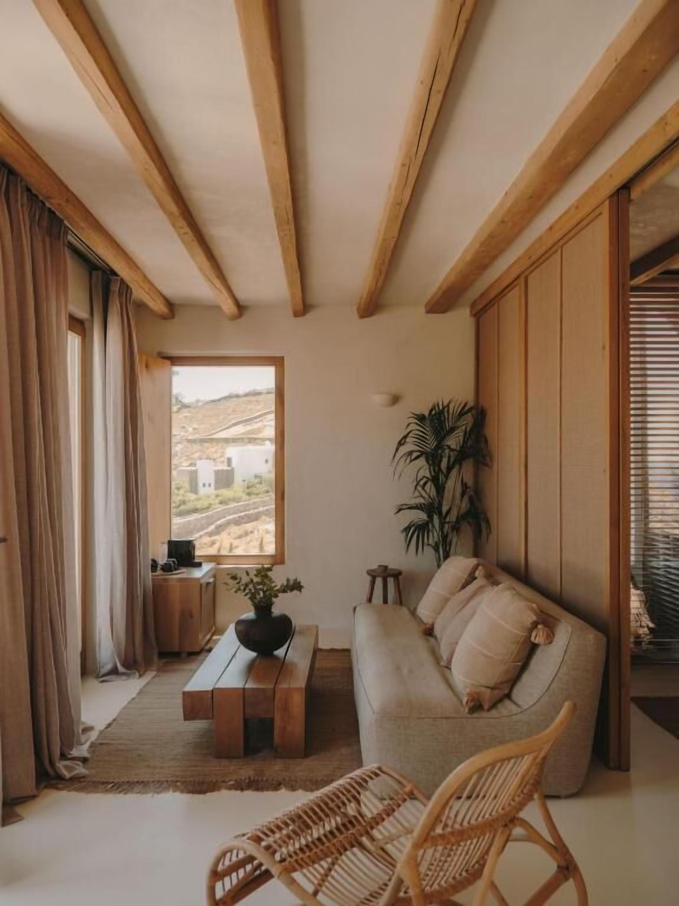 Ein Zimmer mit Holzbalken, einer Couch, einem Couchtisch, einer Pflanze und Blick ins Freie.