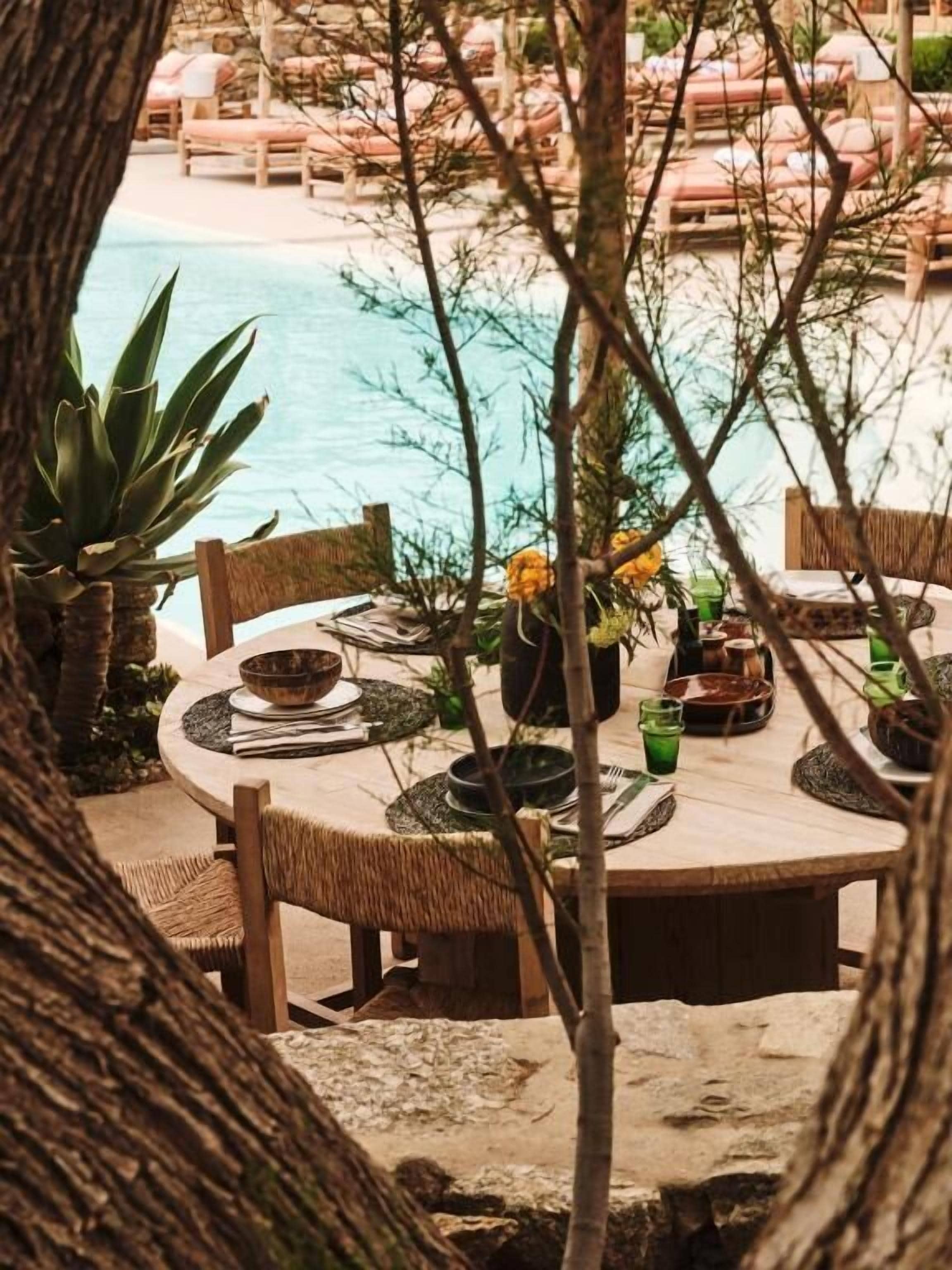 A dining table set outdoors with a view of a pool and beach.