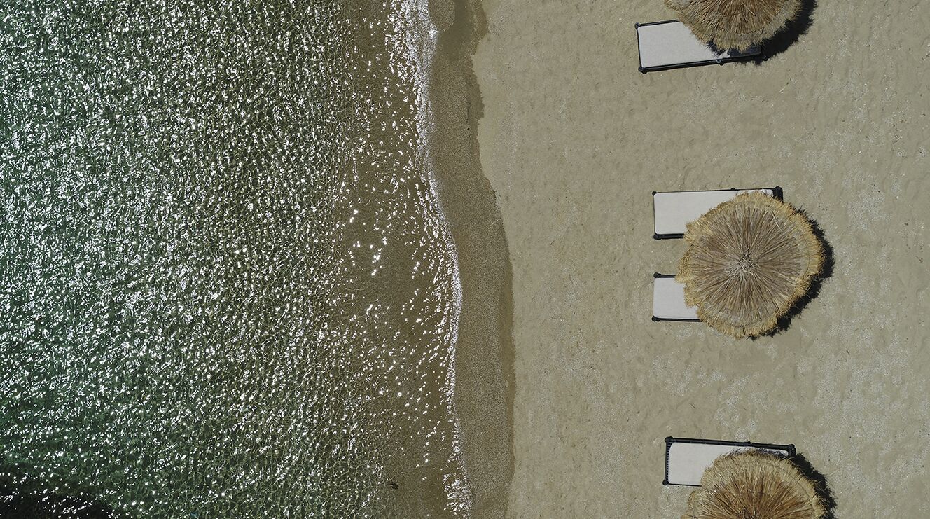 Vista aérea de una playa con tres tumbonas y sombrillas.