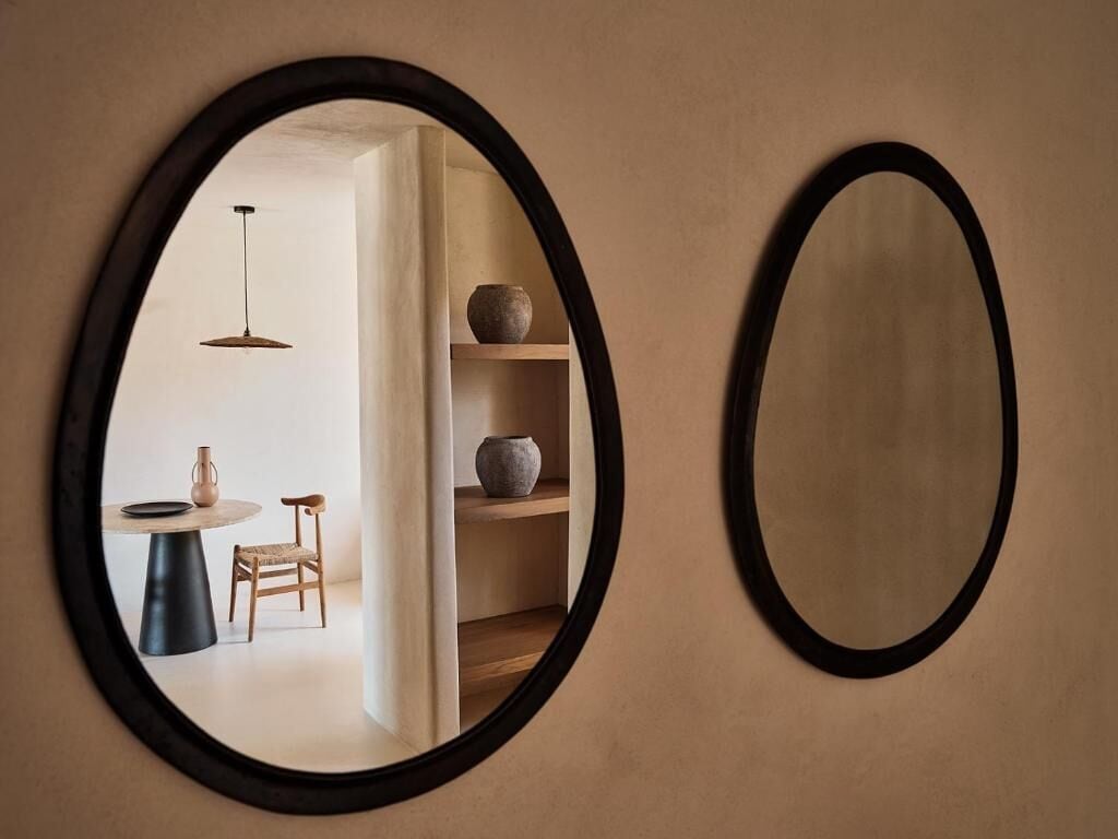Zwei ovale Spiegel an einer Wand, einer zeigt einen Raum mit Tisch, Stuhl und einer Pendelleuchte.