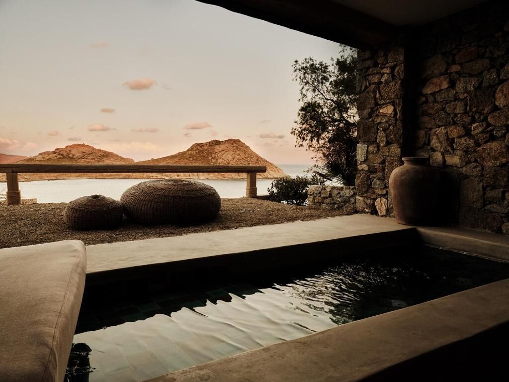 Un muro de piedra, un jarrón grande y una piscina con vistas al mar y las montañas.