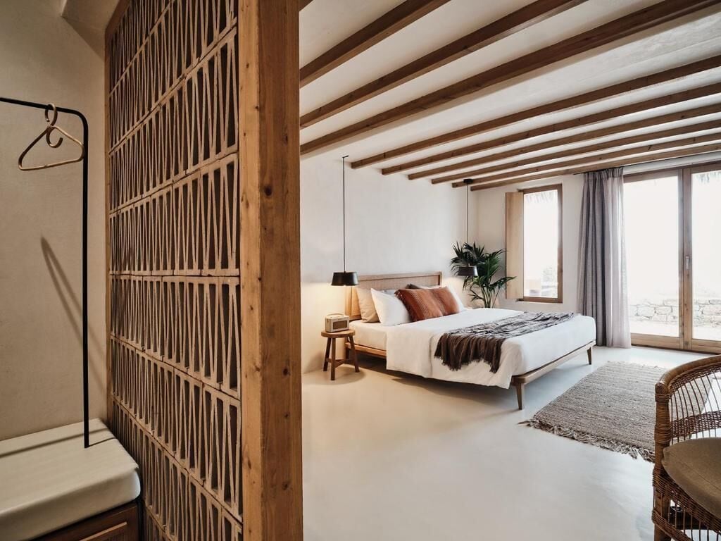 A bedroom with a bed, bedside table, lamp, and a view through a window.