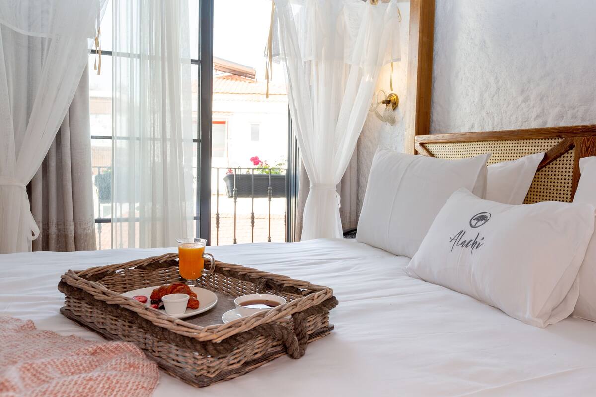 A hotel room with a bed, a wicker tray with breakfast items, and a view of the outside.
