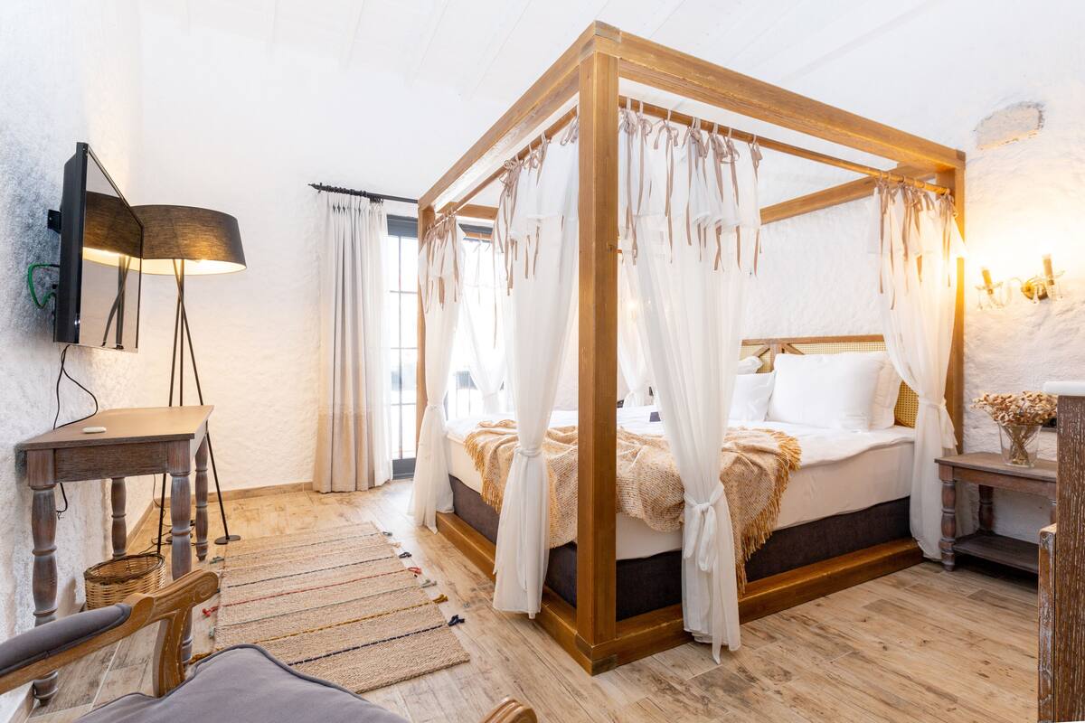 A four-poster bed with white drapes, a wooden headboard, and a bedside table with a lamp.