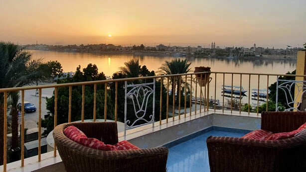 A balcony with wicker chairs and a view of a calm body of water during sunset. - Spring Hotel Luxor (Luxor)