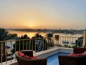 A balcony with wicker chairs and a view of a calm body of water during sunset. - Spring Hotel Luxor (Luxor)