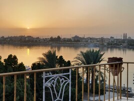 Un balcón con vistas a un paisaje urbano al atardecer, que incluye un río y edificios al fondo.